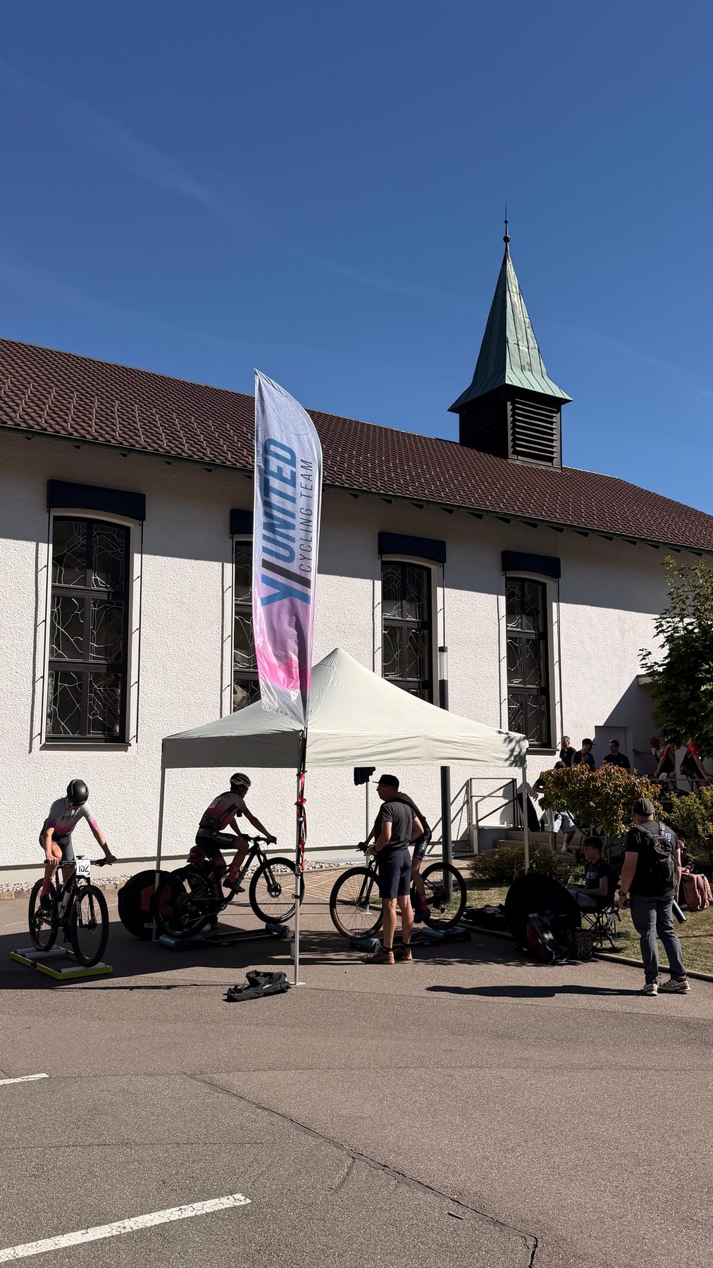 Teamfahne und abgestellte Räder vor einem Gebäude am Rennort Albstadt.