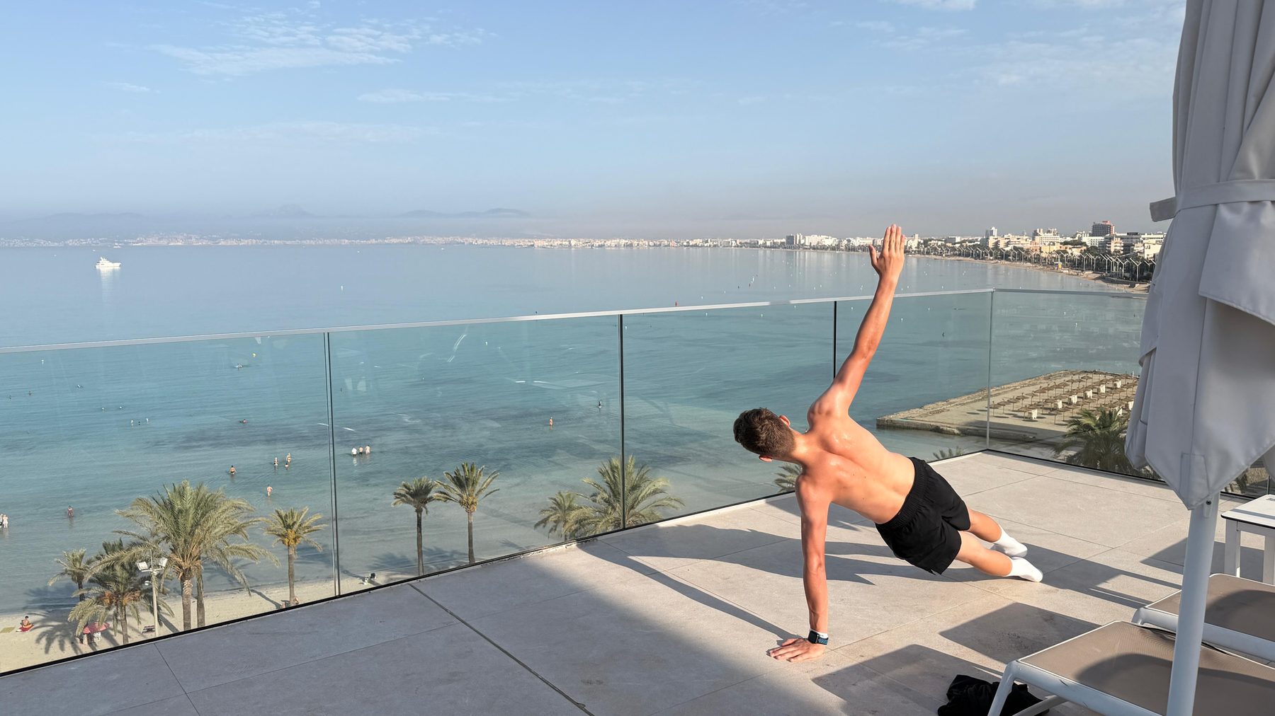 Stabilisationsübung im Handstand auf einer Mauer, dahinter das Meer und ein bewölkter Himmel.